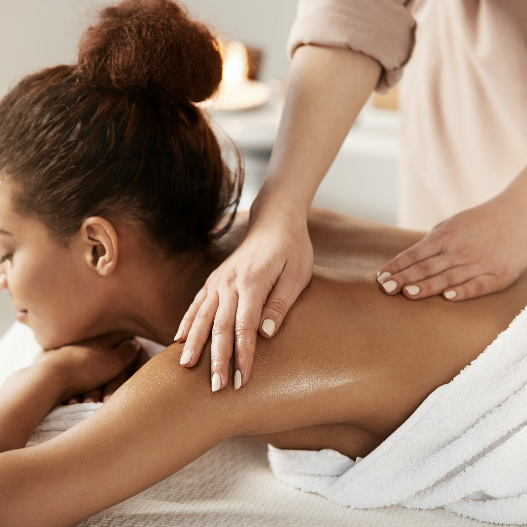 Attractive african girl having massage relaxing in spa salon. Closed eyes.